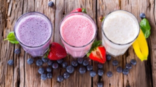 purple, pink and white smoothie on wooden table surrounded by berries